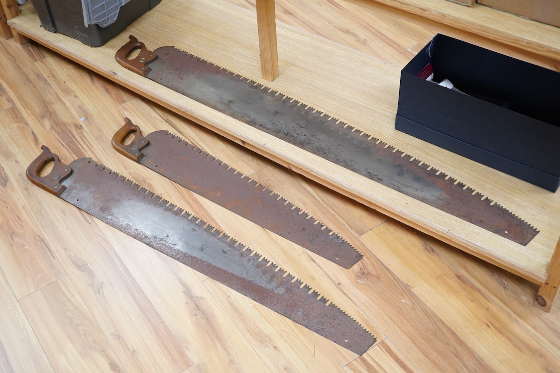 Three large Henry Disston and Sons, Philadelphia, U.S.A. early 20th century hand saws, the largest with a 5’ blade, the makers name still clear on two of the blades, all with similar style wood handles
